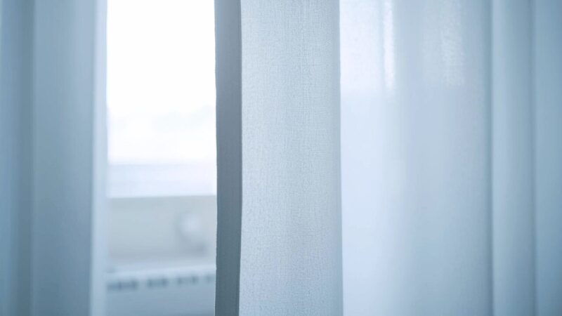 病院の白いカーテンがぼんやり写っており、不安な入院中の雰囲気を表す写真。
