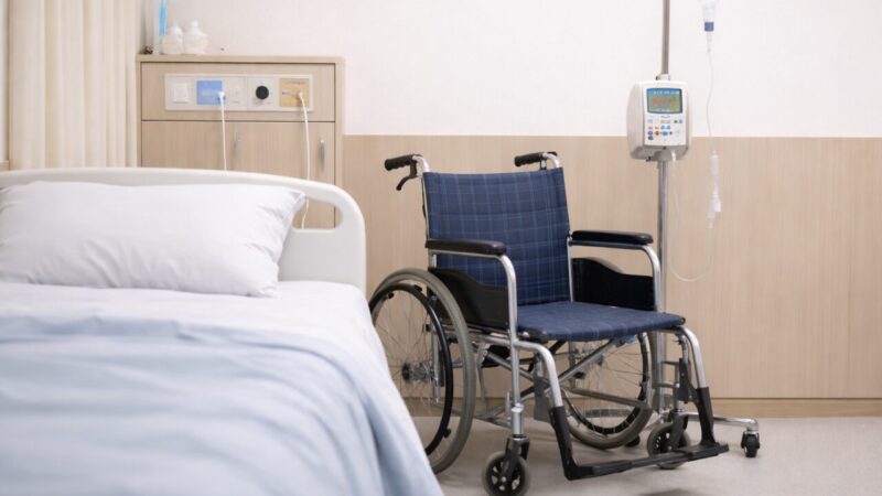 Hospital bed with a wheelchair and IV stand in a quiet hospital room
