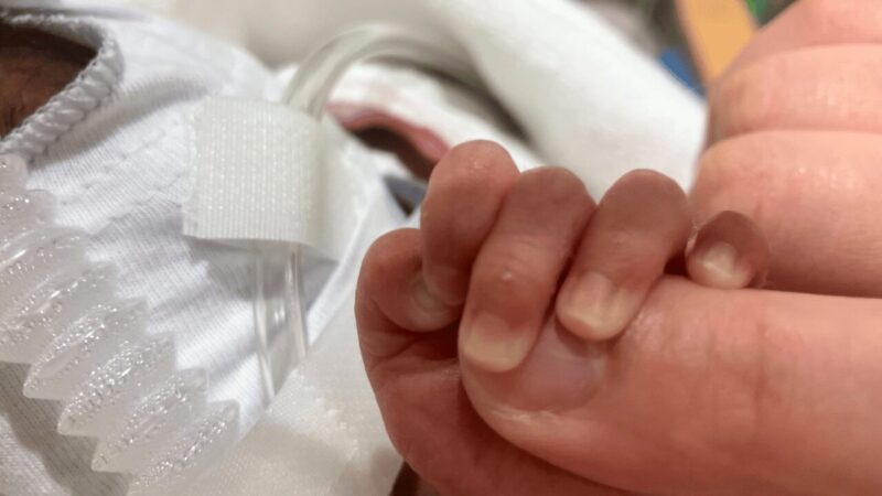 NICUで小さな赤ちゃんが母の指を握っている写真。
